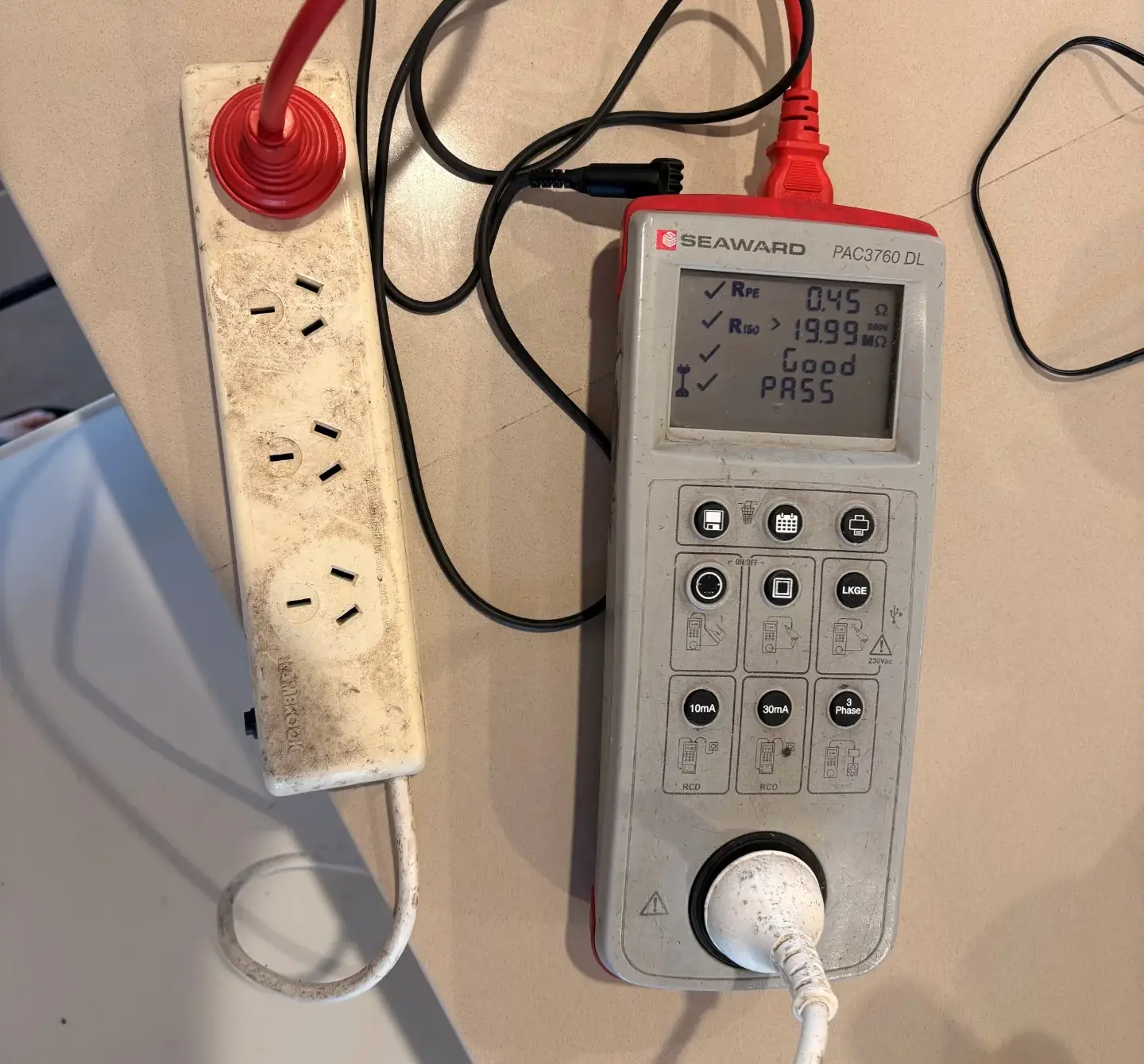 Portable appliance tester showing a PASS result while testing a workshop power board