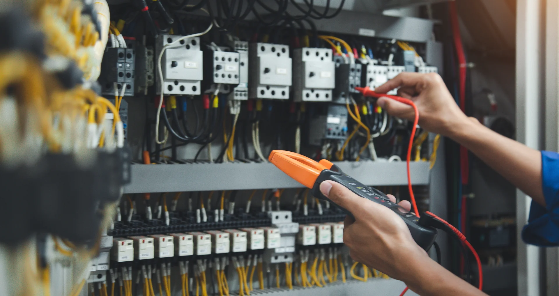 Technician testing circuit breakers in an industrial control cabinet with a voltage tester